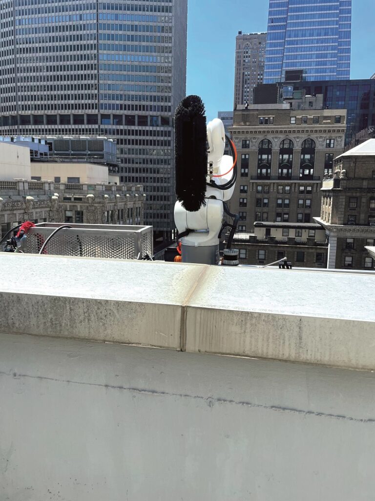 The Ozmo’s brush seen over the roof parapet of a tall building, with its Ouster Lidar visible lower right. The brush includes water distribution nozzles (Courtesy of Skyline Robotics)